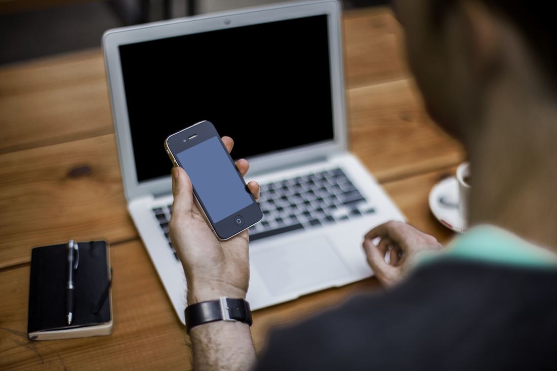 Person seen from behind with a smartphone and laptop at a work table
